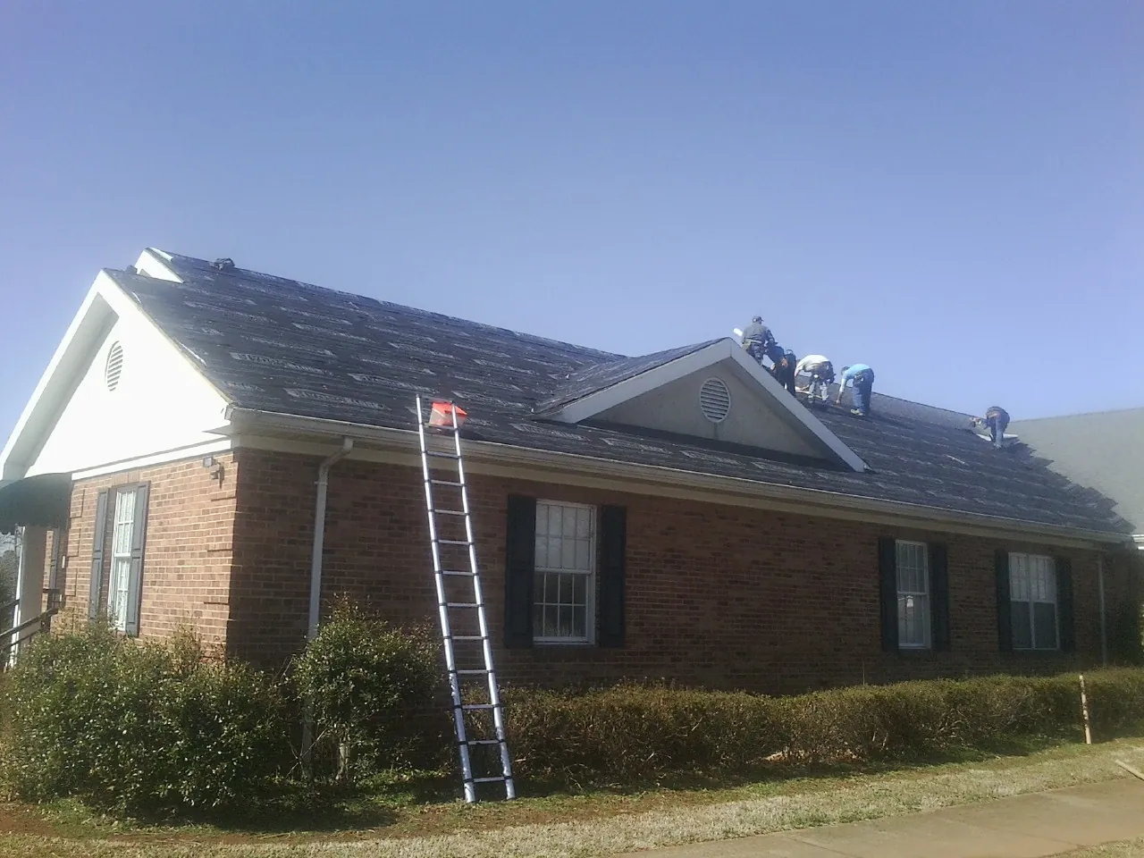 Crew tearing shingles off a brick ranch roof with a ladder set — Emergency Roof Repair work by our crew in Jobstown