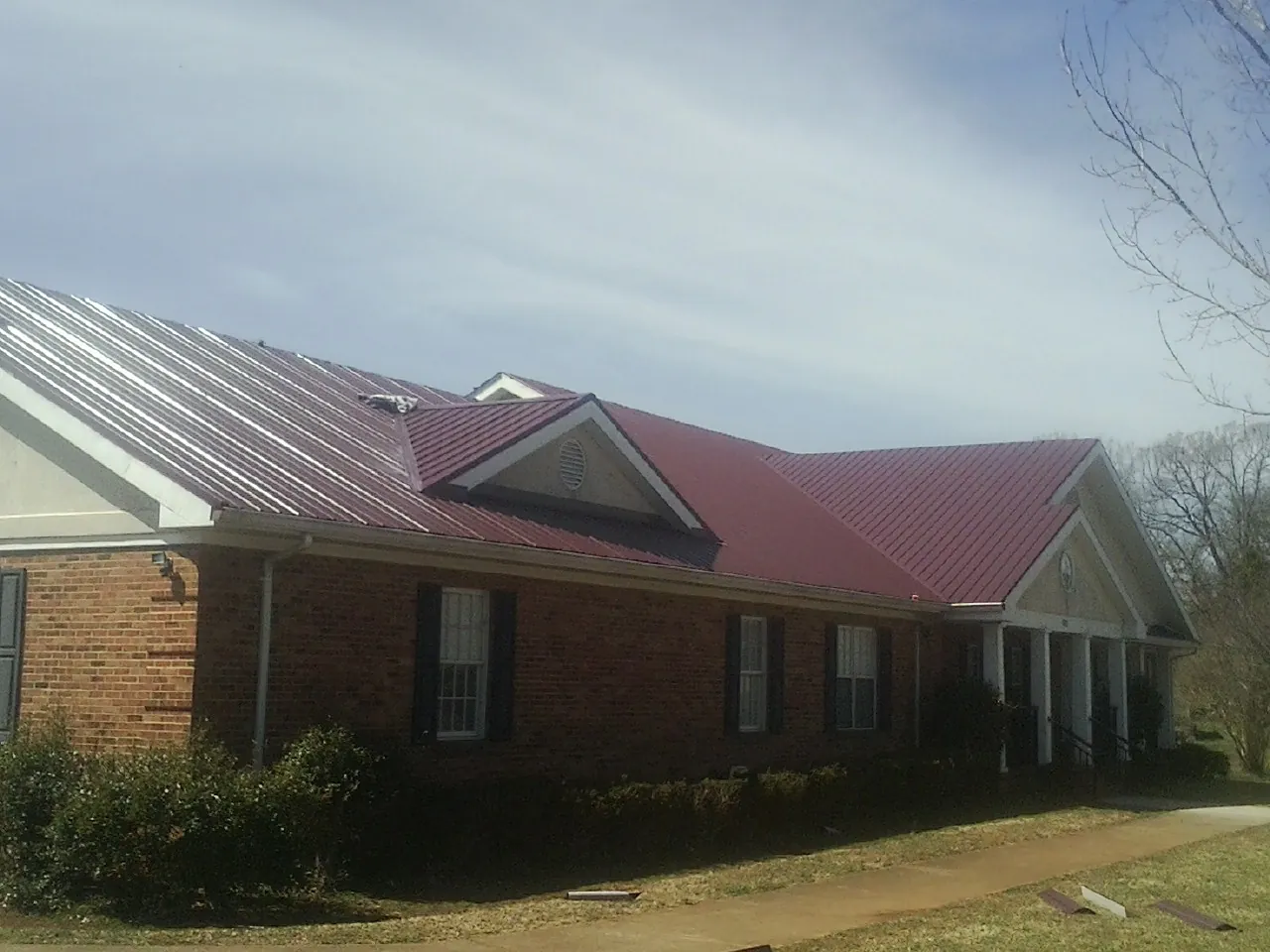Red metal roof with gabled entries on a long brick building, from a Hail Damage Roof Repair job in Jobstown