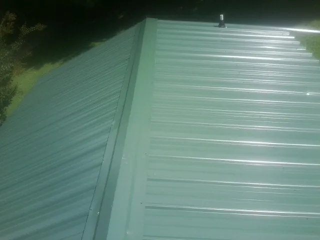 New green metal panels meeting at the ridge of a roof — Flat Roof Repair work by our crew in Jobstown