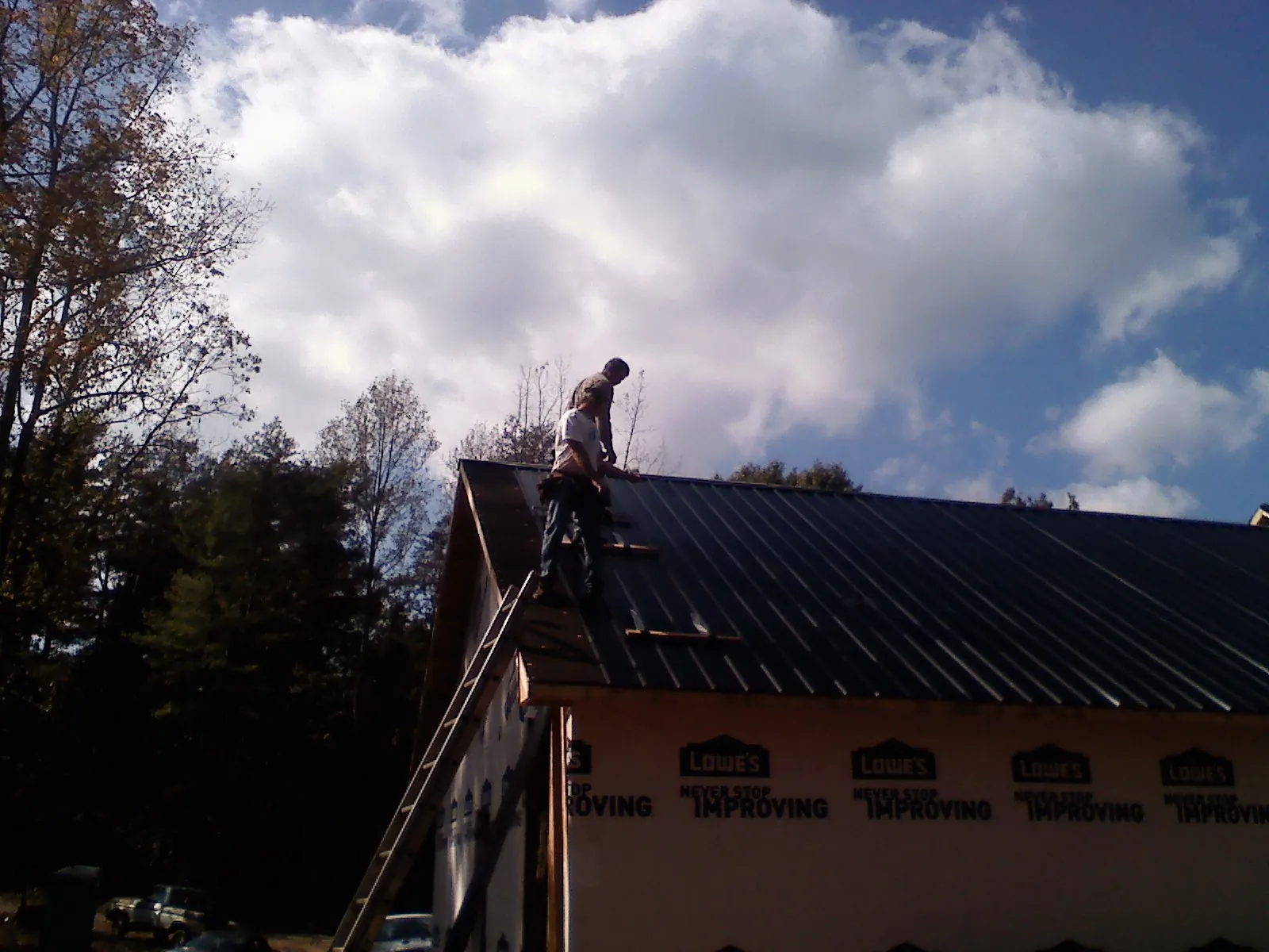 Roofer fastening dark metal panels high against a cloudy sky, from a Roof Inspection job in Jobstown