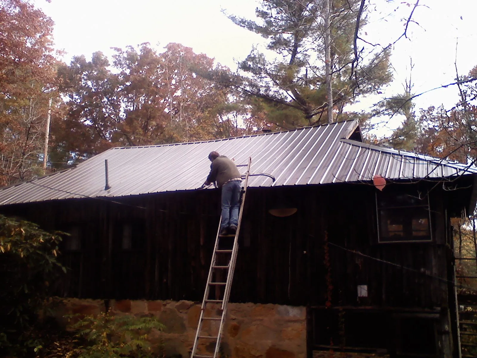 Roofer on a ladder working along the edge of a cabin metal roof in Jobstown