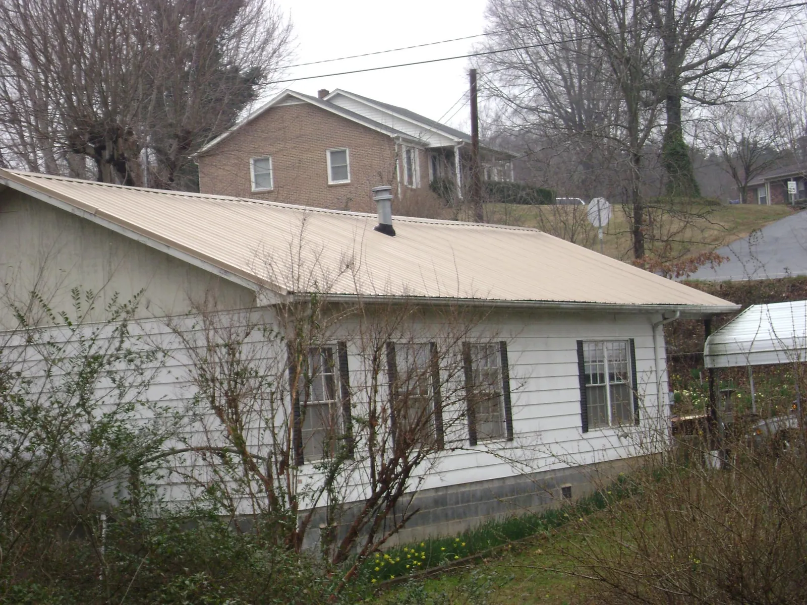 Tan metal roof on a white sided house set into a hillside — Commercial Roofing by Roofing Brothers in Jobstown